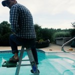 Harvey holds a camera, sitting atop a painter's ladder in the shallow end of a saltwater pool.
